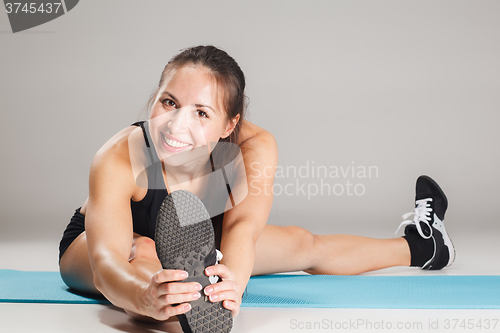 Image of Muscular young woman athlete stretching on gray 