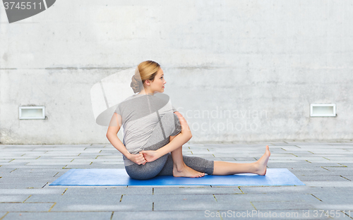 Image of woman making yoga in twist pose on mat outdoors