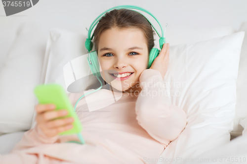 Image of happy girl lying in bed with smartphone at home