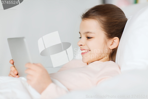 Image of happy girl lying in bed with tablet pc at home