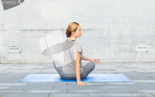 Image of woman making yoga in twist pose on mat outdoors