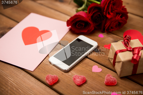 Image of close up of smartphone, gift, red roses and hearts