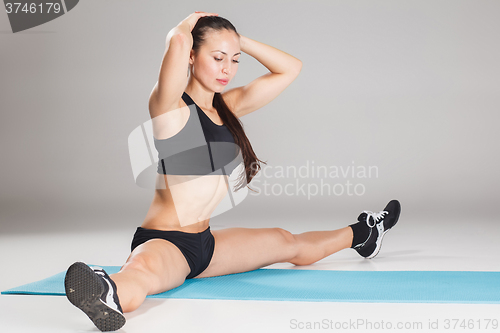 Image of Muscular young woman athlete stretching on gray 