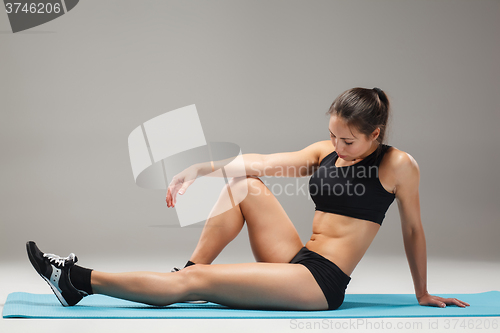Image of Muscular young woman athlete stretching on gray 