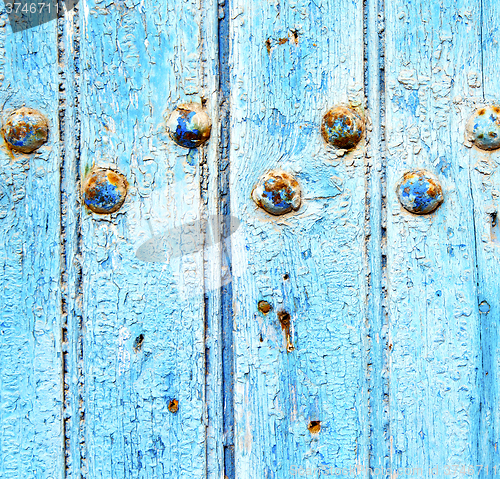 Image of stripped paint in the blue wood door and rusty nail