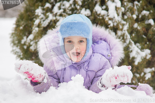 Image of Girl lying in the snow the snow with snowballs in hand