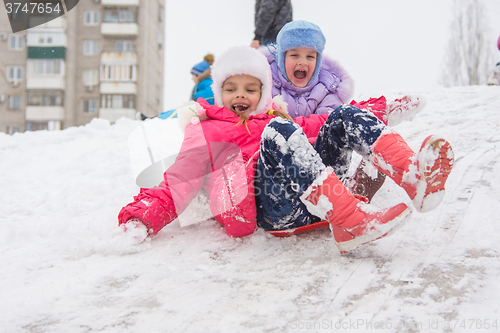 Image of Two happy girls slide down the icy hill