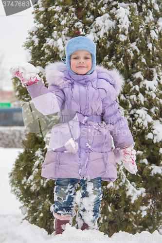 Image of Girl standing on a snowbank snow with snowball in hand