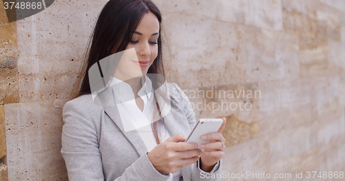 Image of Female worker texting and leaning against wall