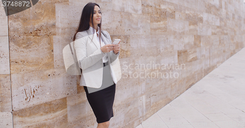 Image of Female worker texting and leaning against wall