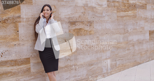 Image of Pretty woman talking on phone and leaning on wall