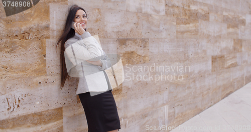 Image of Happy woman talking on phone and leaning on wall