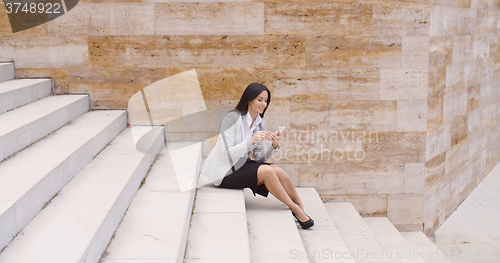 Image of Pretty business woman sitting on steps using phone