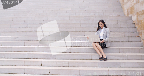 Image of Pretty young worker sitting on steps with laptop