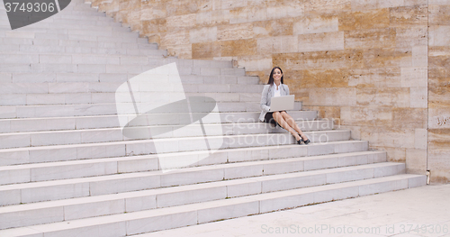 Image of Pretty young worker sitting on steps with laptop