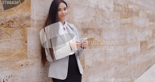 Image of Business woman leaning against wall texting