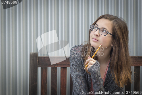 Image of Young Daydreaming Female Student With Pencil Looking to the Side