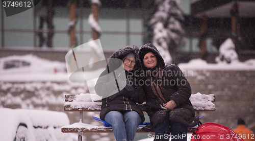 Image of portrait of two mature woman sitting in park at  winter day