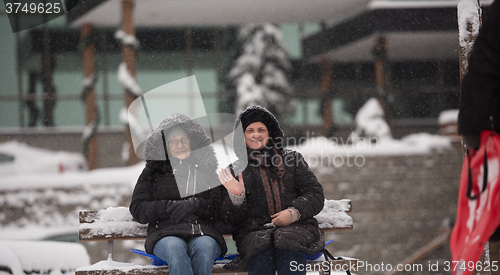 Image of portrait of two mature woman sitting in park at  winter day