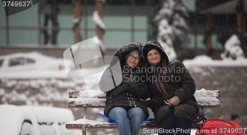 Image of portrait of two mature woman sitting in park at  winter day