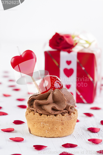 Image of cup-cake with cherry in front of gift box 