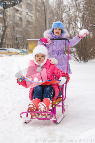 Image of The girls in the courtyard of riding a snow sled rejoice