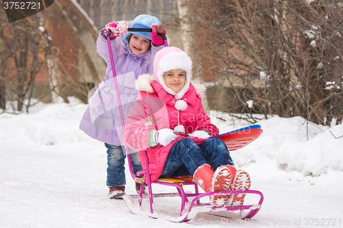 Image of The girl rolls the other girl on a sled in the yard