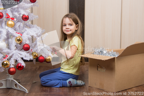 Image of Funny girl takes off a Christmas tree with toys