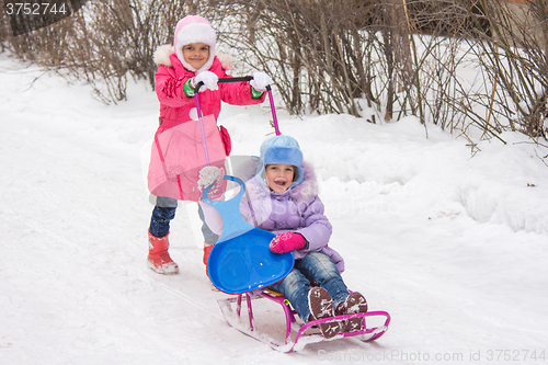 Image of The older girl rolls the younger girl on a sled in the yard