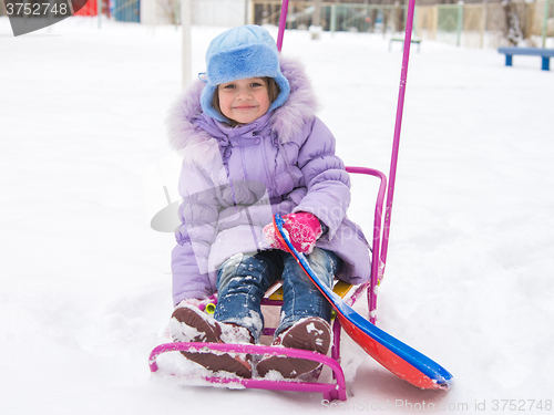 Image of Joyful girl sitting on a sled in the snowy weather