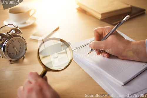 Image of The male hands with a pencil and magnifying glass