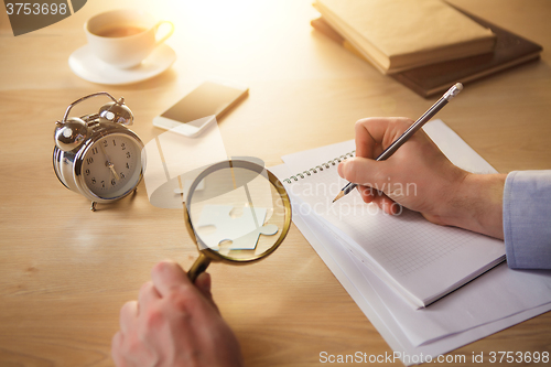 Image of The male hands with a pencil and magnifying glass