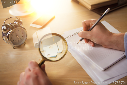 Image of The male hands with a pencil and magnifying glass