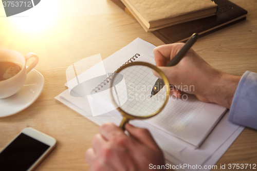 Image of The male hands with a pencil and magnifying glass