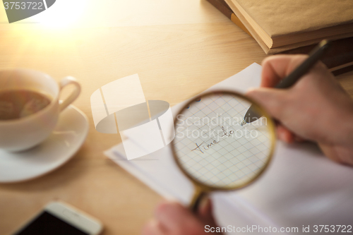 Image of The male hands with a pencil and magnifying glass