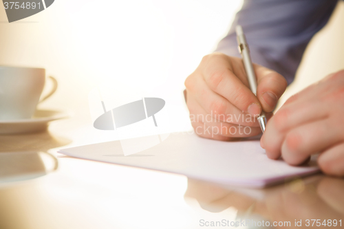 Image of The male hand with a pen and the cup