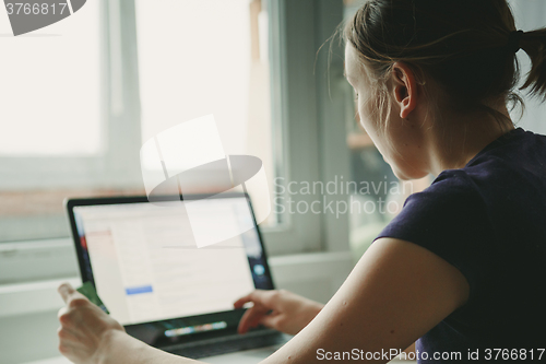 Image of Woman working with laptop placed on wooden desk