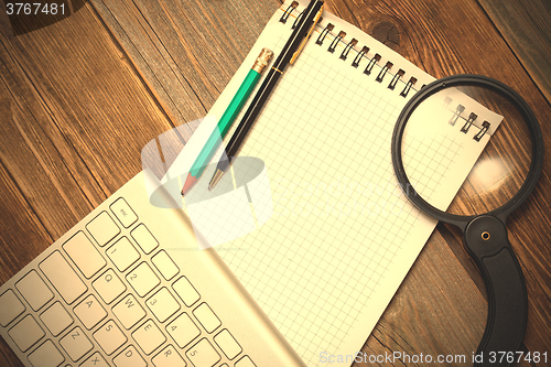 Image of notebook, computer keyboard, magnifying glass and a pencil with 