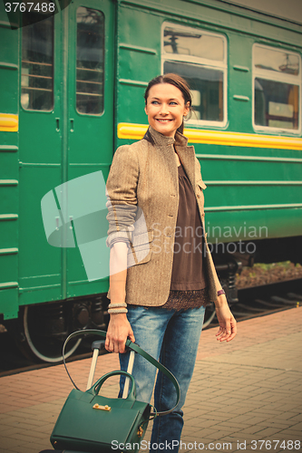 Image of smiling beautiful middle-aged woman with luggage on a railway pl