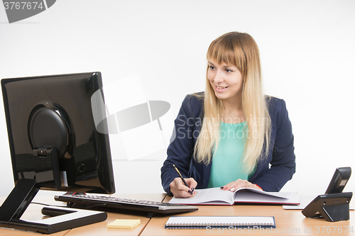 Image of Business woman writing in a business book and looked at the computer monitor