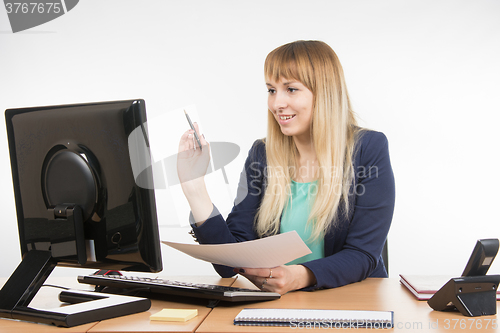 Image of Happy business woman working at a computer and holding a piece of paper and a pen