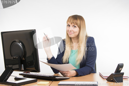 Image of Business woman holding a sheet of paper and a pen and working on the computer in the office