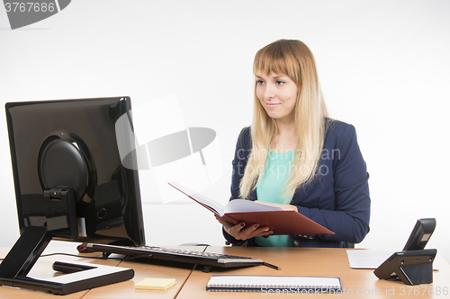 Image of Happy business woman holding a book in the hands of the office and looking at the computer