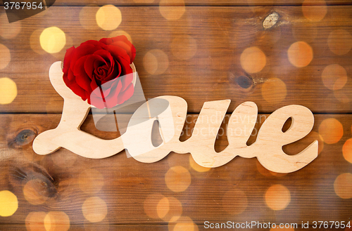 Image of close up of word love cutout with red rose on wood