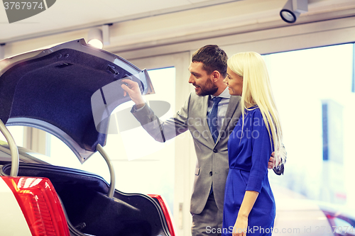 Image of happy couple with car dealer in auto show or salon