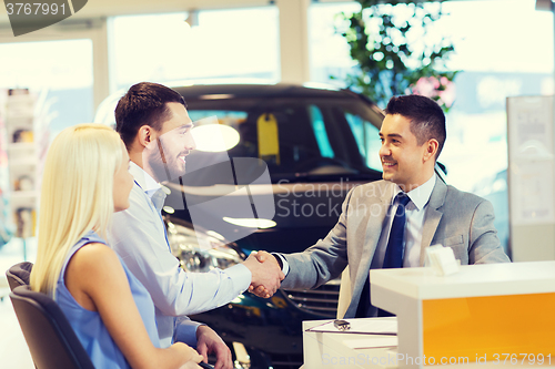 Image of happy couple with car dealer in auto show or salon