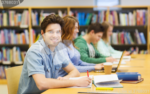 Image of happy student boy with books writing in library