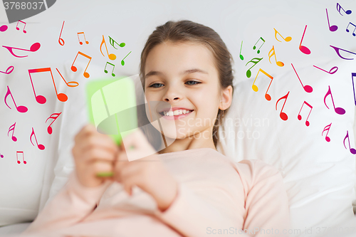 Image of happy girl lying in bed with smartphone over notes