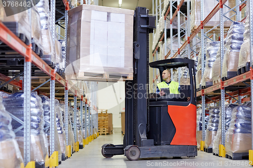 Image of man with tablet pc operating forklift at warehouse