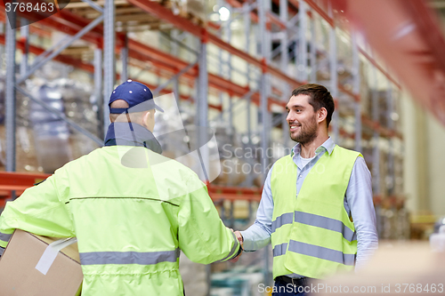 Image of men in safety vests shaking hands at warehouse